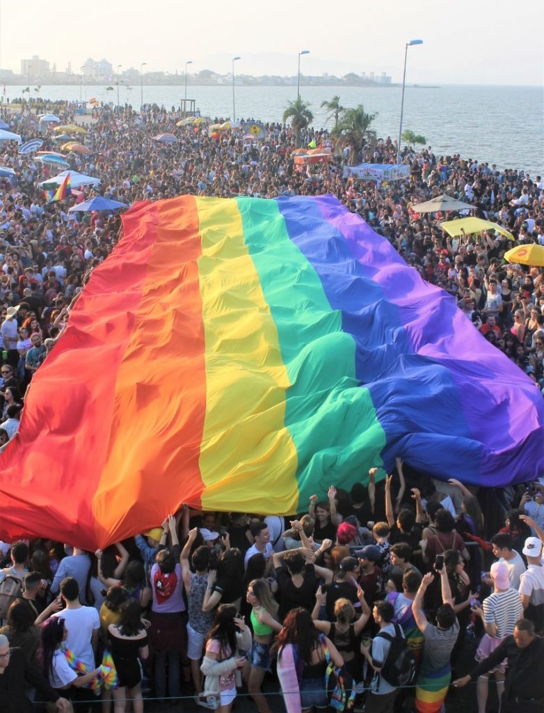 Uma multidão ergue uma bandeira com as cores o arco-íris gigante