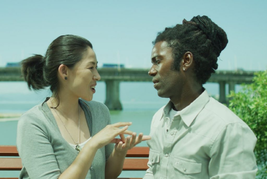 Uma mulher branca de descendência asiática conversa com um homem negro em um banco de madeira