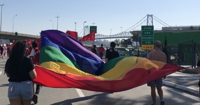 Manifestantes levam bandeira colorida que representa a comunidade LGBTQ+ em uma manifestação