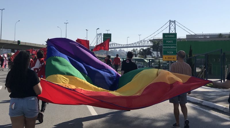 Manifestantes levam bandeira colorida que representa a comunidade LGBTQ+ em uma manifestação